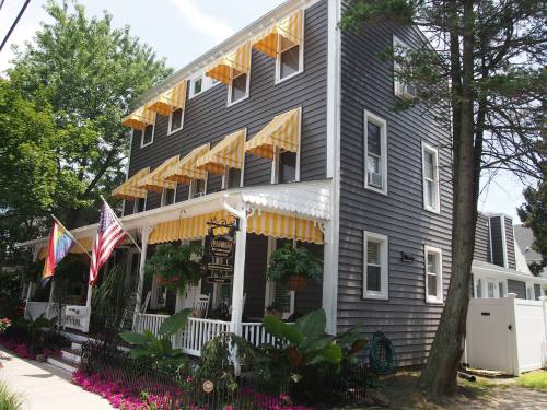 A charming gray house with yellow awnings, surrounded by greenery and flowers, featuring American flags on the porch.