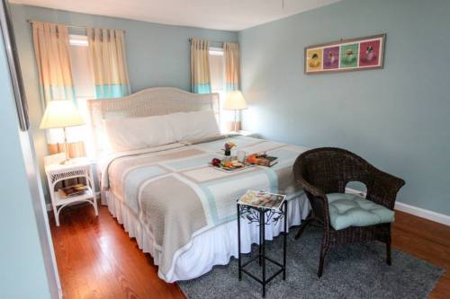 Cozy bedroom with a large bed, two lamps, a wicker chair, and a small table with snacks, featuring light blue walls.
