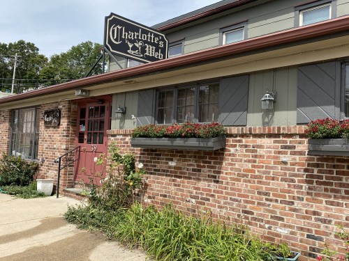 Exterior of a brick building with a sign reading "Charlotte's Web," featuring flower boxes and a welcoming entrance.