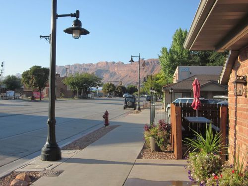 A quiet street view with a lamp post, fire hydrant, and mountains in the background under a clear blue sky.