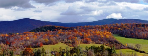 A scenic view of rolling hills covered in vibrant autumn foliage under a cloudy sky.