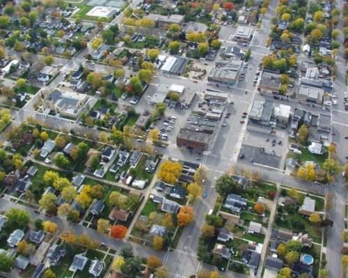 Aerial view of a suburban neighborhood with trees changing colors, streets, and a mix of residential and commercial buildings.