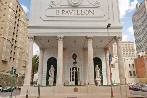 Exterior view of Le Pavillon hotel, featuring grand columns, statues, and a classic architectural design.