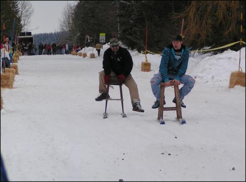 Two people sitting on stools on a snowy track, preparing for a race, with spectators in the background.