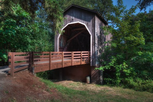 A rustic wooden covered bridge surrounded by lush greenery and trees.