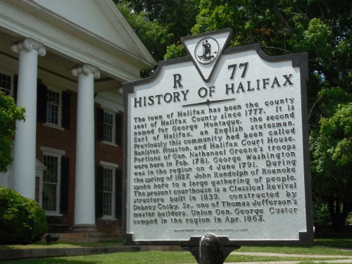 Historical marker about Halifax County, detailing its history and notable figures, set against a colonial-style building.
