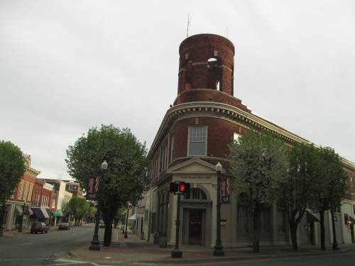 Historic brick building with a round tower, situated at a street corner, surrounded by trees and empty sidewalks.