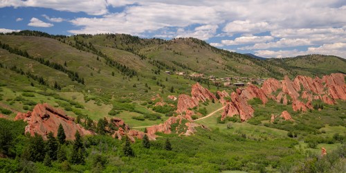 A scenic view of red rock formations surrounded by green hills and trees under a partly cloudy sky.