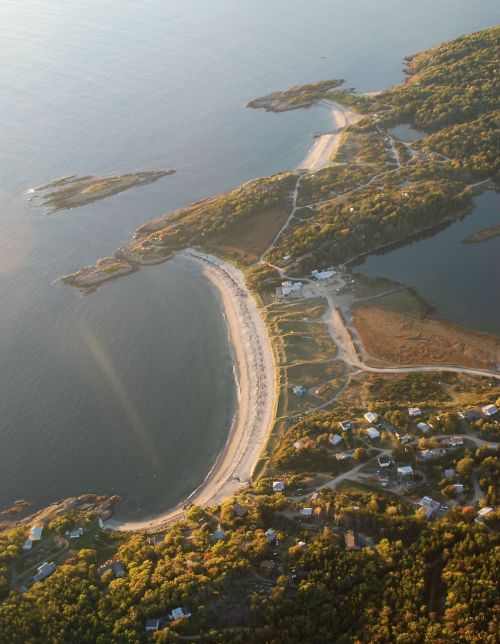 Aerial view of a curved beach surrounded by greenery and water, with small islands in the distance.