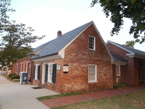 A brick building with a sloped roof, featuring blue shutters and a mailbox outside, set in a grassy area.