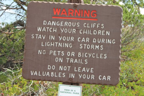 A warning sign in a national park advises about dangerous cliffs, staying in cars during storms, and pet restrictions.