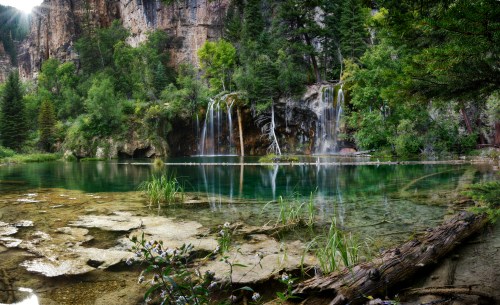 A serene landscape featuring a clear lake surrounded by lush greenery and cascading waterfalls in a rocky setting.