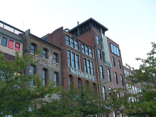 Historic brick buildings with a sign for McFadden's, surrounded by greenery and a clear blue sky.