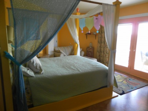 A cozy bedroom with a four-poster bed, colorful decor, and large windows letting in natural light.