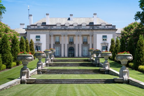 A grand mansion with a symmetrical facade, surrounded by manicured lawns and decorative flower planters.