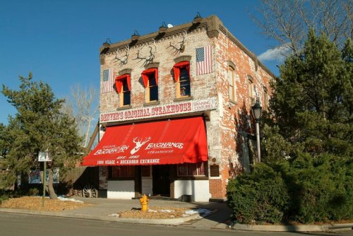 Historic brick building with a red awning, featuring flags and antlers, housing a steakhouse in a small town.