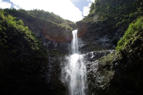 A majestic waterfall cascading down a rocky cliff, surrounded by lush green hills under a bright sky.