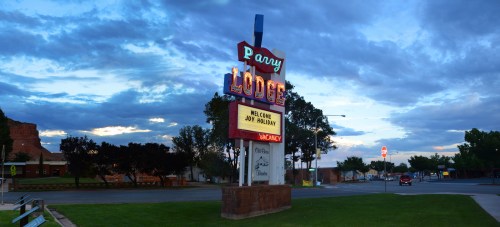 Sign for Parry Lodge at dusk, featuring "Welcome Joy Valley" and a vintage neon design against a cloudy sky.