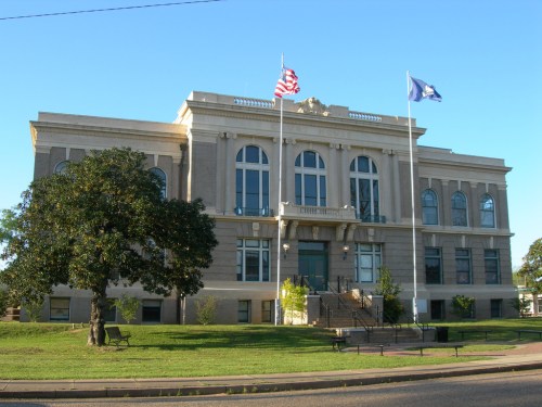 Historic building with large windows, two flags flying, and a green lawn in front. Clear blue sky above.