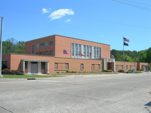 A brick building with multiple windows, flags, and a clear blue sky in the background.