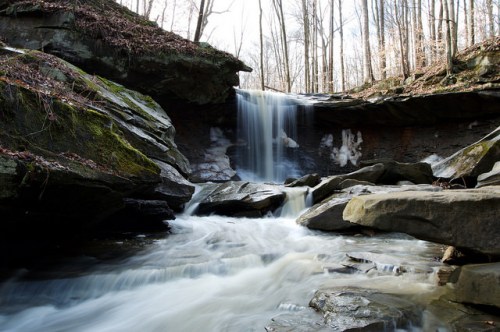 A serene waterfall cascades over rocks, surrounded by trees in a tranquil forest setting.