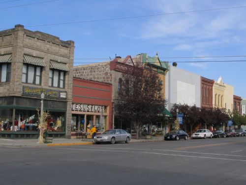 A quaint street scene featuring historic buildings, shops, and parked cars under a clear blue sky.