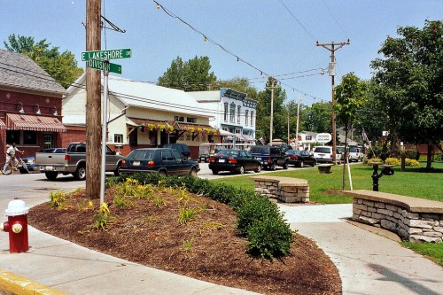 A quaint street scene with shops, parked cars, and greenery, featuring a street sign for Lakeshore and Division.