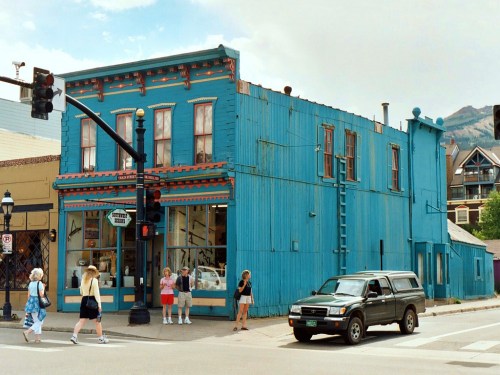 A vibrant blue building with decorative trim, pedestrians walking nearby, and a car stopped at a traffic light.
