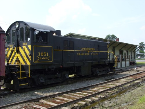 A black and yellow locomotive parked at a train station, with tracks and a building in the background.
