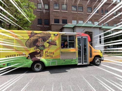 A colorful food truck named "Flour Tacos" parked on a street, with a vendor visible at the window.