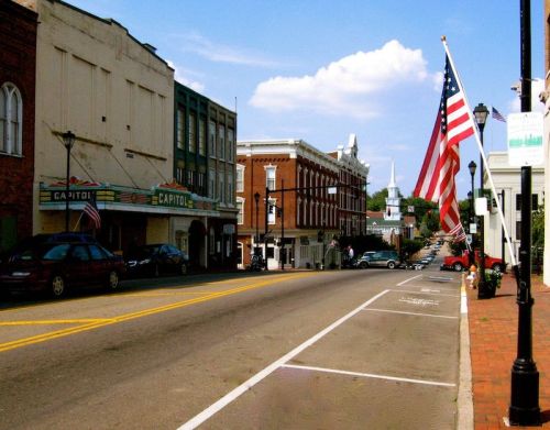A quiet street scene featuring historic buildings, an American flag, and a church steeple in the background.
