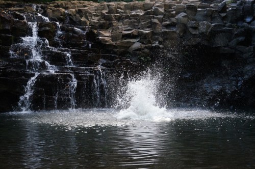 A waterfall cascades over rocky cliffs into a serene pool, creating a splash in the water below.
