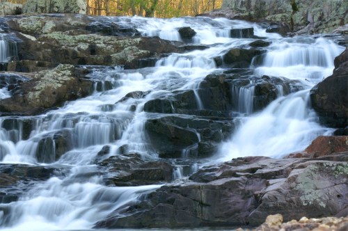 A serene waterfall cascading over rocky terrain, surrounded by lush greenery and soft sunlight.