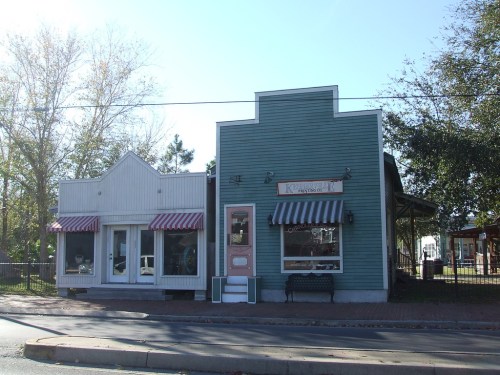 Two quaint storefronts with colorful awnings, one white and one teal, set against a clear blue sky.