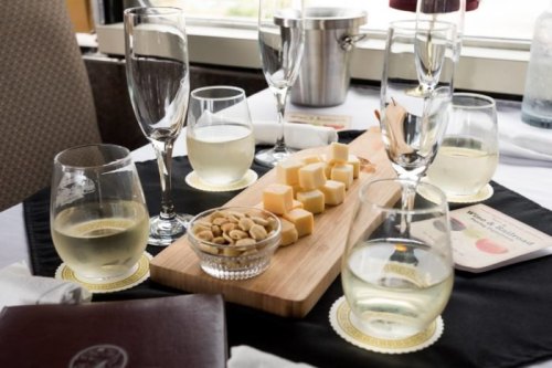 A table setting with glasses of white wine, a cheese platter, nuts, and elegant tableware.