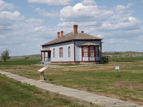 Historic building with a red and white exterior, surrounded by grassy fields and under a partly cloudy sky.