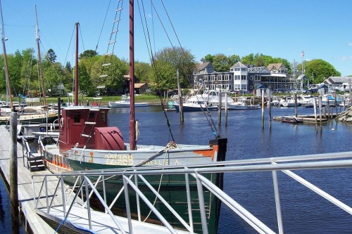 A red boat docked at a marina with green trees and buildings in the background under a clear blue sky.