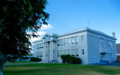 Historic school building with a large entrance, surrounded by grass and trees under a blue sky.
