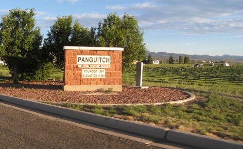 Sign for Panguitch, Utah, established in 1884, with elevation noted as 6,680 feet, surrounded by green fields.