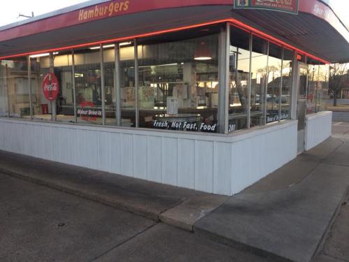 A retro hamburger restaurant with large windows, featuring a Coca-Cola sign and a "Fresh, Not Fast, Food" slogan.