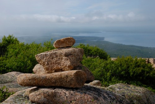A stack of rocks on a hillside, overlooking a misty landscape and water in the distance.