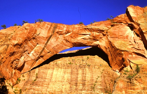 A natural rock arch set against a clear blue sky, showcasing vibrant red and orange sandstone formations.