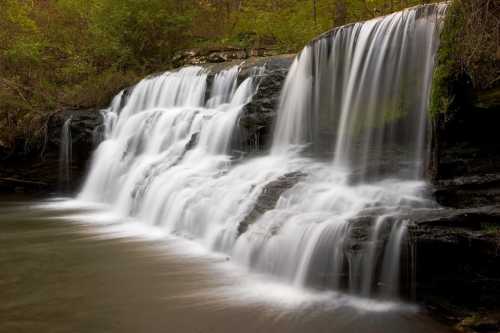 A serene waterfall cascading over rocks, surrounded by lush greenery and a calm pool below.