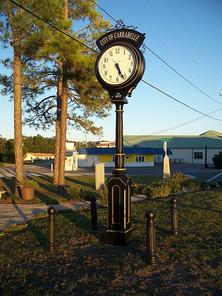 A vintage clock tower in Carrabelle, Florida, surrounded by trees and a clear blue sky.