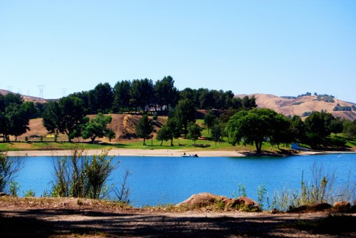 A serene lake surrounded by green trees and rolling hills under a clear blue sky.