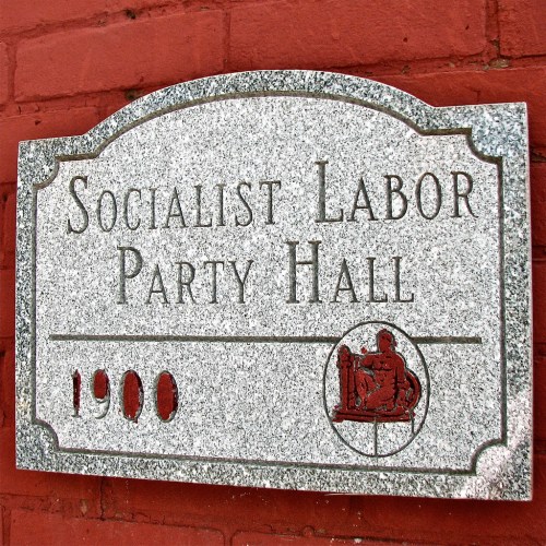 A stone plaque reading "Socialist Labor Party Hall" with the year "1900" engraved below it, mounted on a red brick wall.