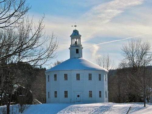 A round white building with a cupola, surrounded by snow and trees, under a clear blue sky.