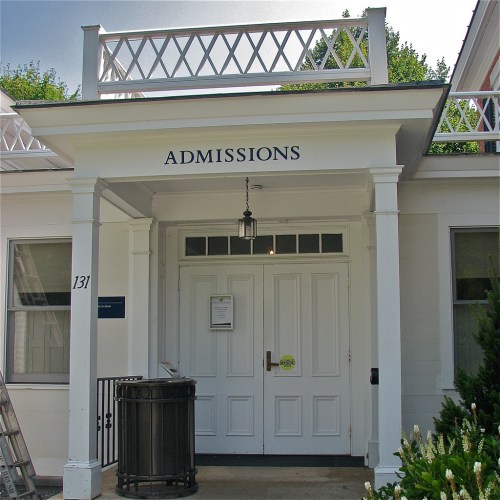 Entrance to an admissions building with a sign above the door, featuring white columns and a lantern.