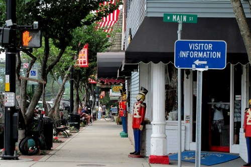 A street scene featuring shops, a visitor information sign, and decorative figures along the sidewalk.