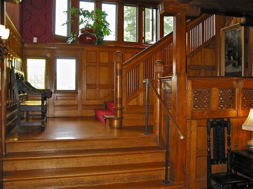 A wooden staircase leads to an upper level in a warmly lit, vintage-style entryway with decorative paneling.